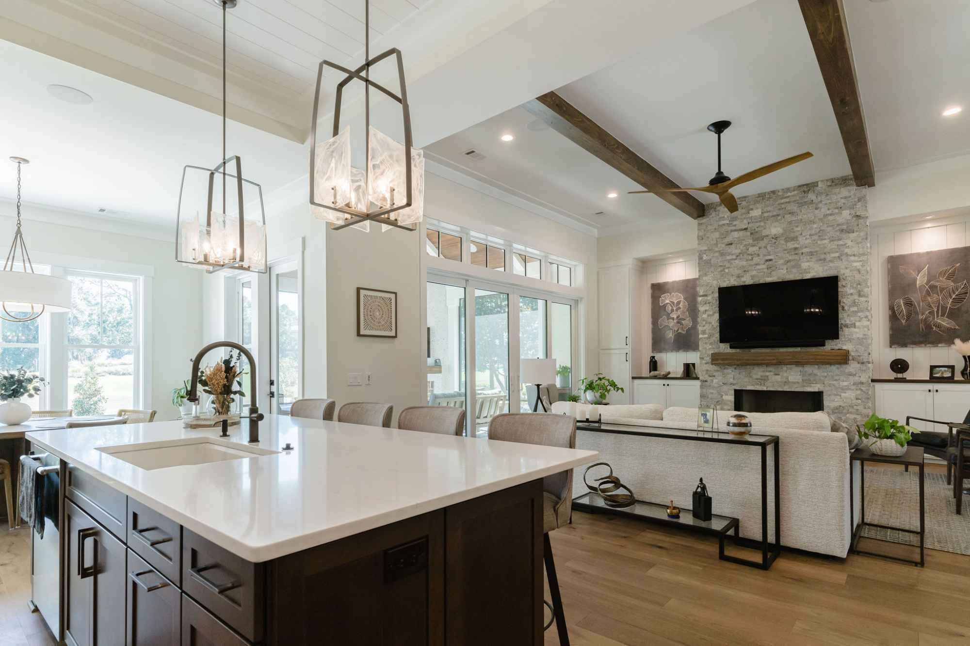 This photograph shows a modern open-plan living and kitchen area. The kitchen features a large island with a sink and pendant lighting, while the living room has a fireplace, television and comfortable seating.