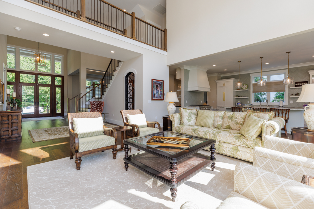 A bright and airy living room featuring a high ceiling, a balcony overlooking the livving room and a view of the entrance and the kitchen.