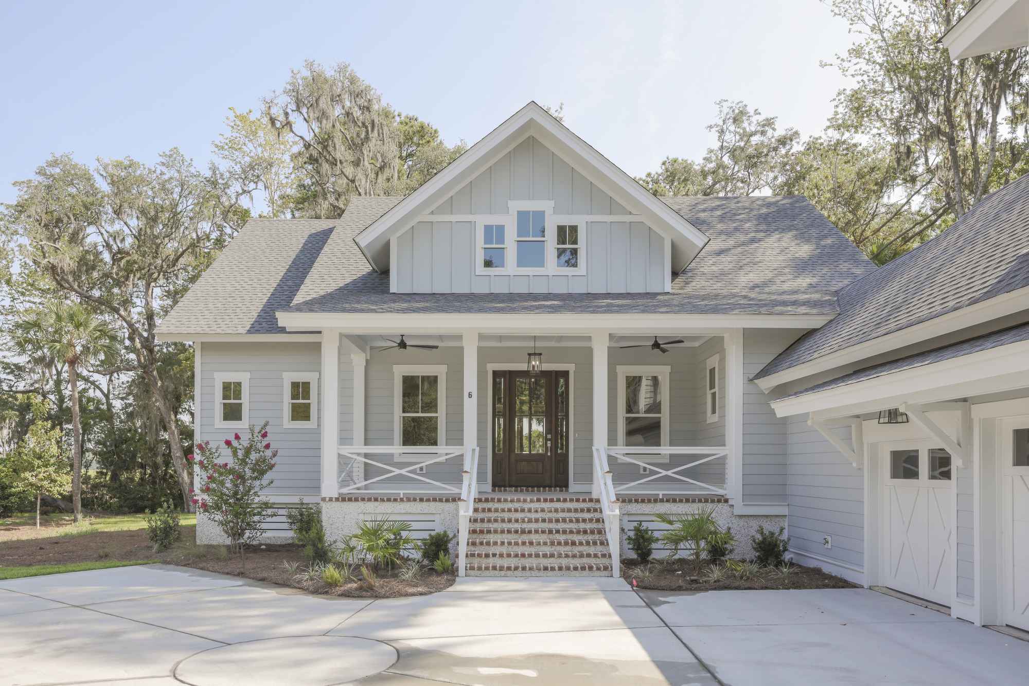 Charming two-story gray house with a gabled roof, white trim, and a welcoming porch surrounded by trees, under a clear blue sky.