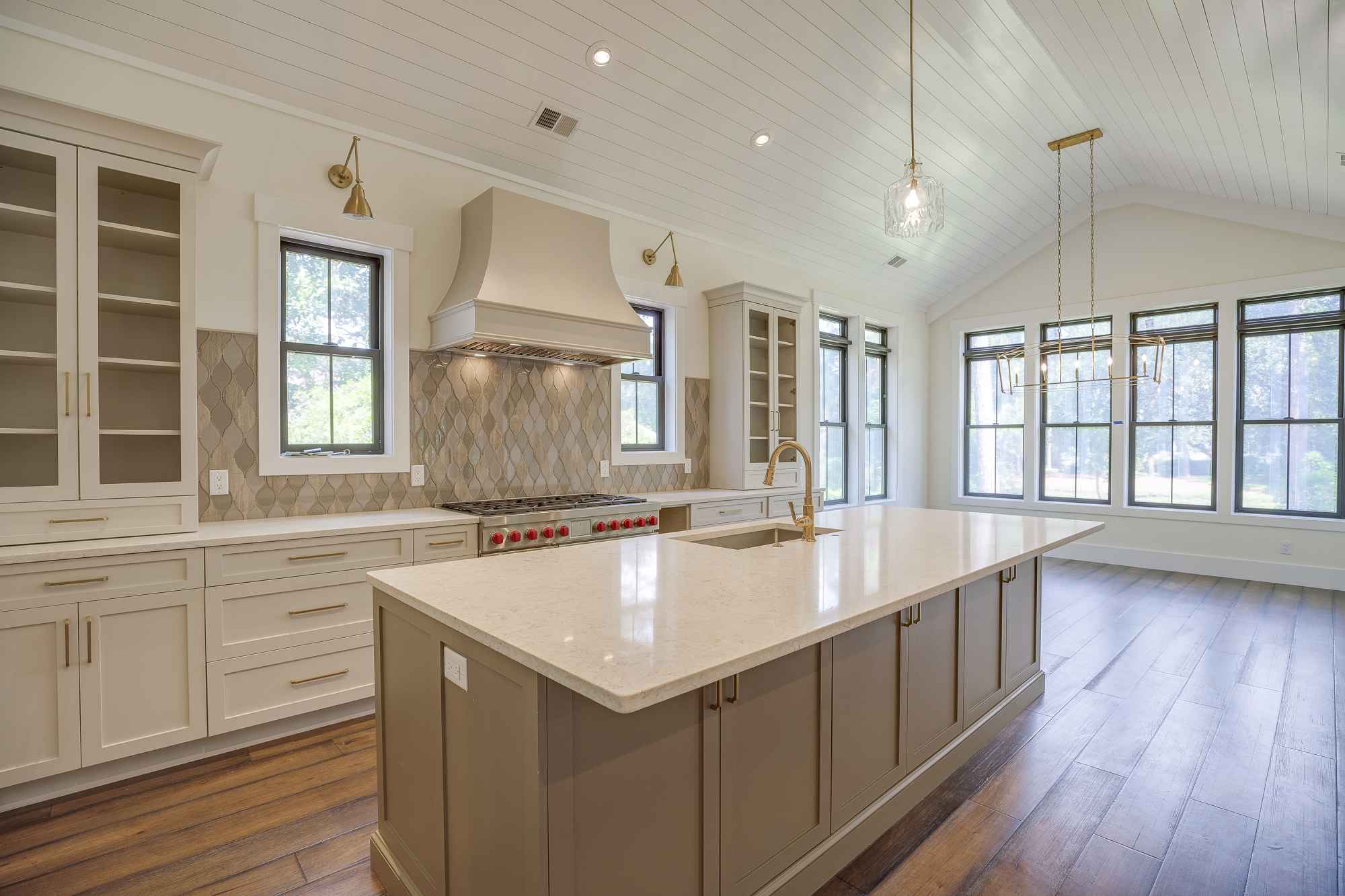 Spacious, modern kitchen with high ceilings and large windows. Central island with light countertops, elegant cabinetry, and warm wooden floors.