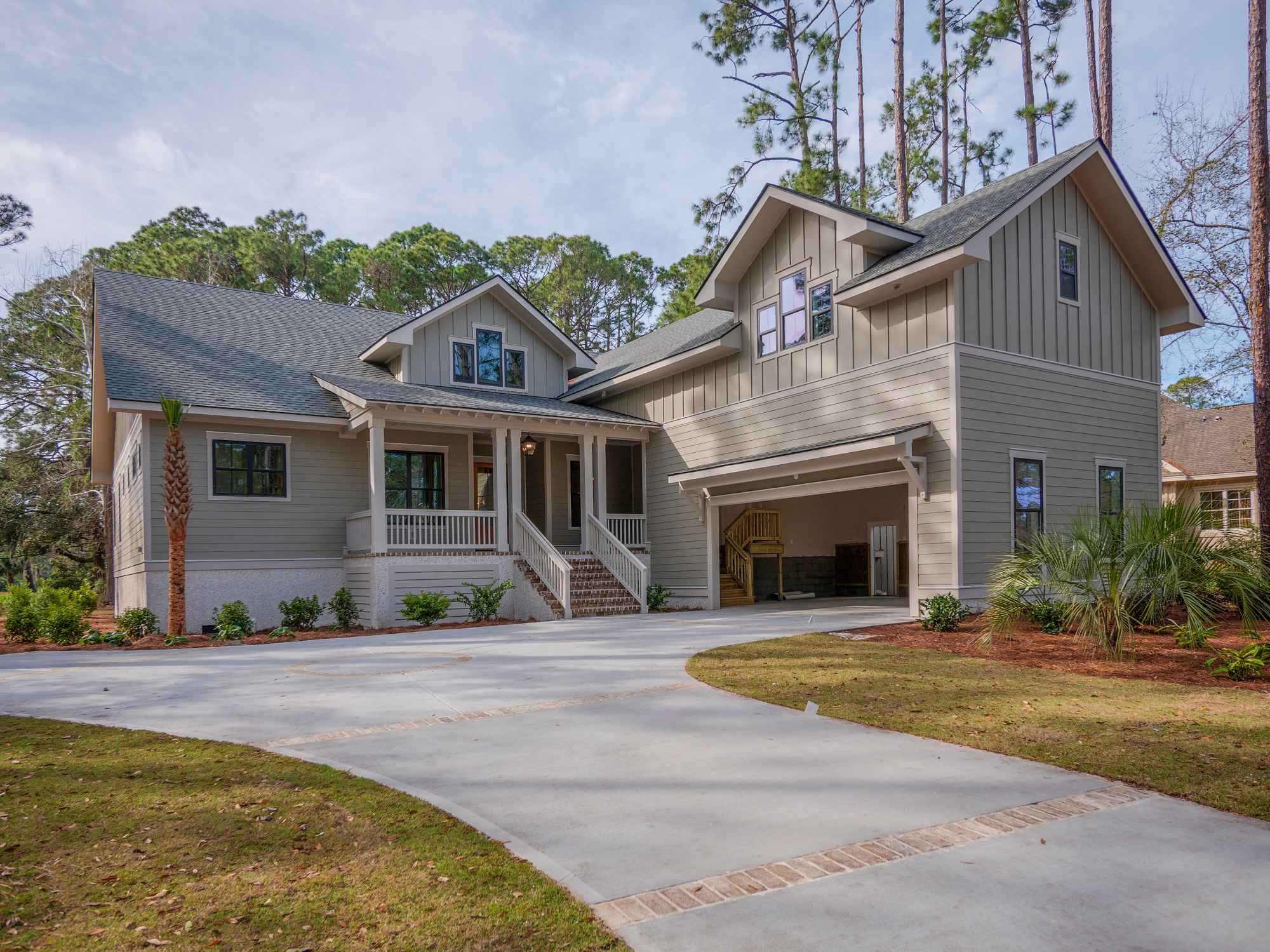Charming two-story home with gray siding, a gabled roof, and attached garage. Surrounded by tall trees, lush landscaping, and a well-maintained driveway.