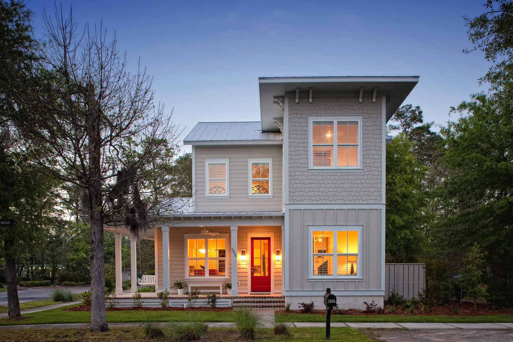 Charming two-story house with lit windows, a bold red door, and a wraparound porch.