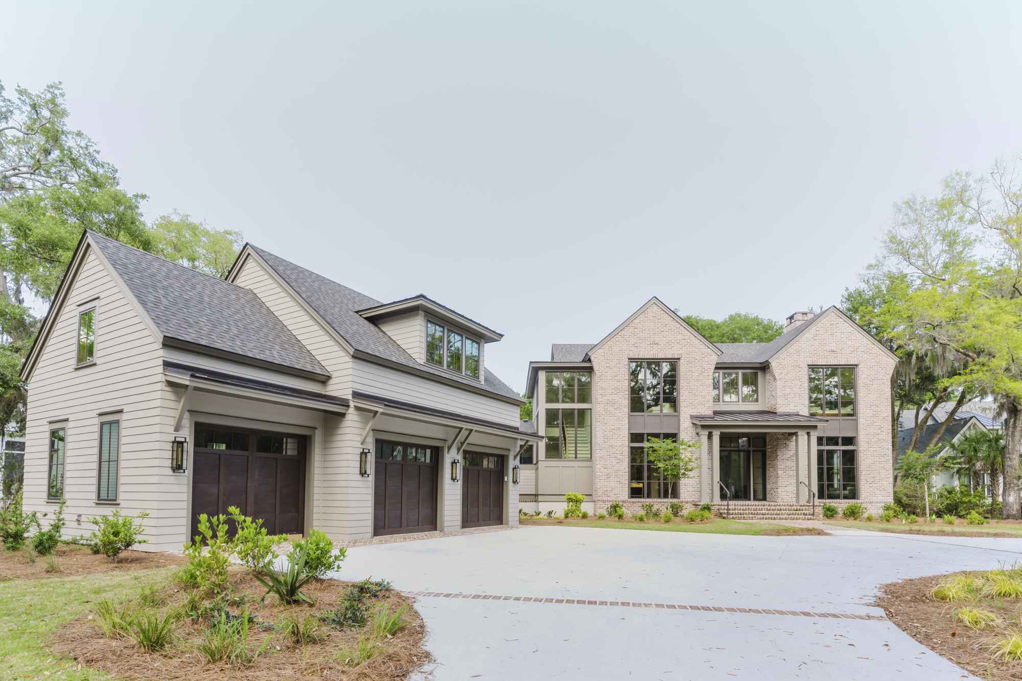 A spacious, modern two-story house with a large driveway, gabled roofs, and a three-car garage, surrounded by greenery and a clear sky.
