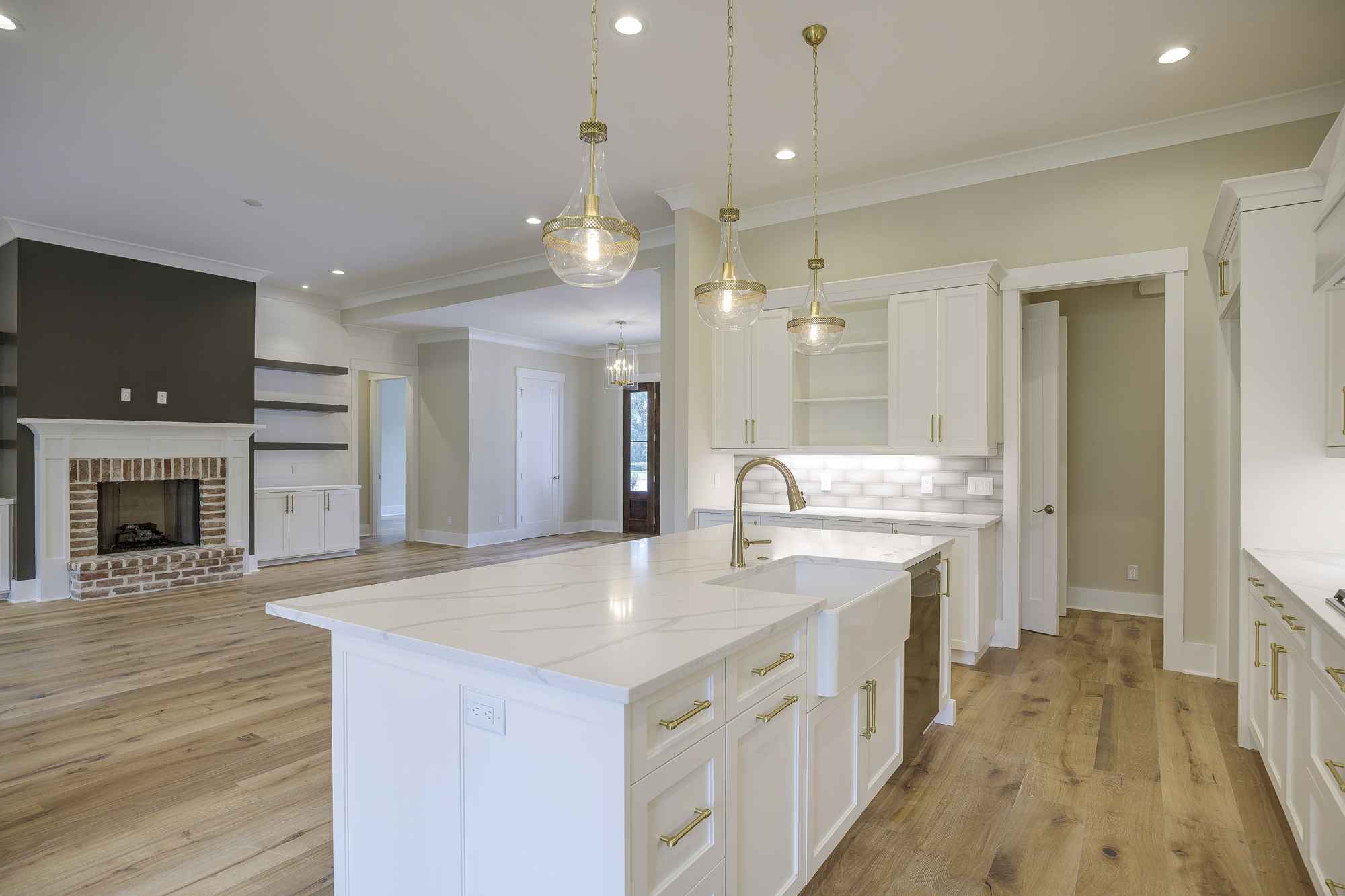 Spacious kitchen with white cabinets, center island, and pendant lights; open to a cozy living area with a brick fireplace and built-in shelves.