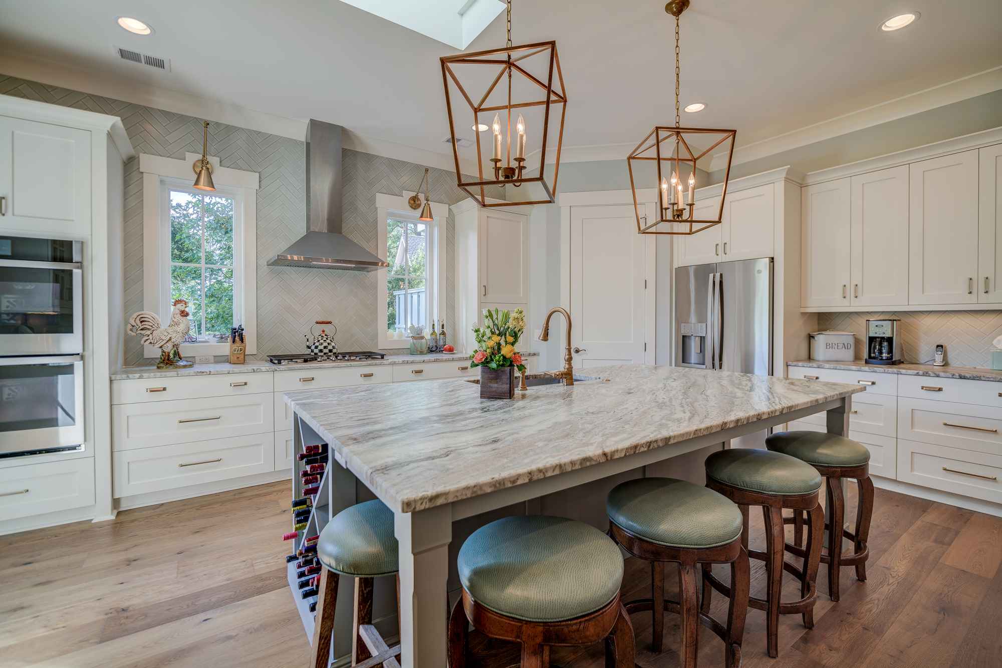 Spacious kitchen with a large marble island, four cushioned stools, white cabinets, stainless steel appliances, and pendant lights.