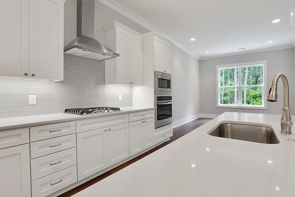 Spacious modern kitchen with white cabinets, stainless steel appliances, and a large island with a sink. Bright, natural light streams through a window.