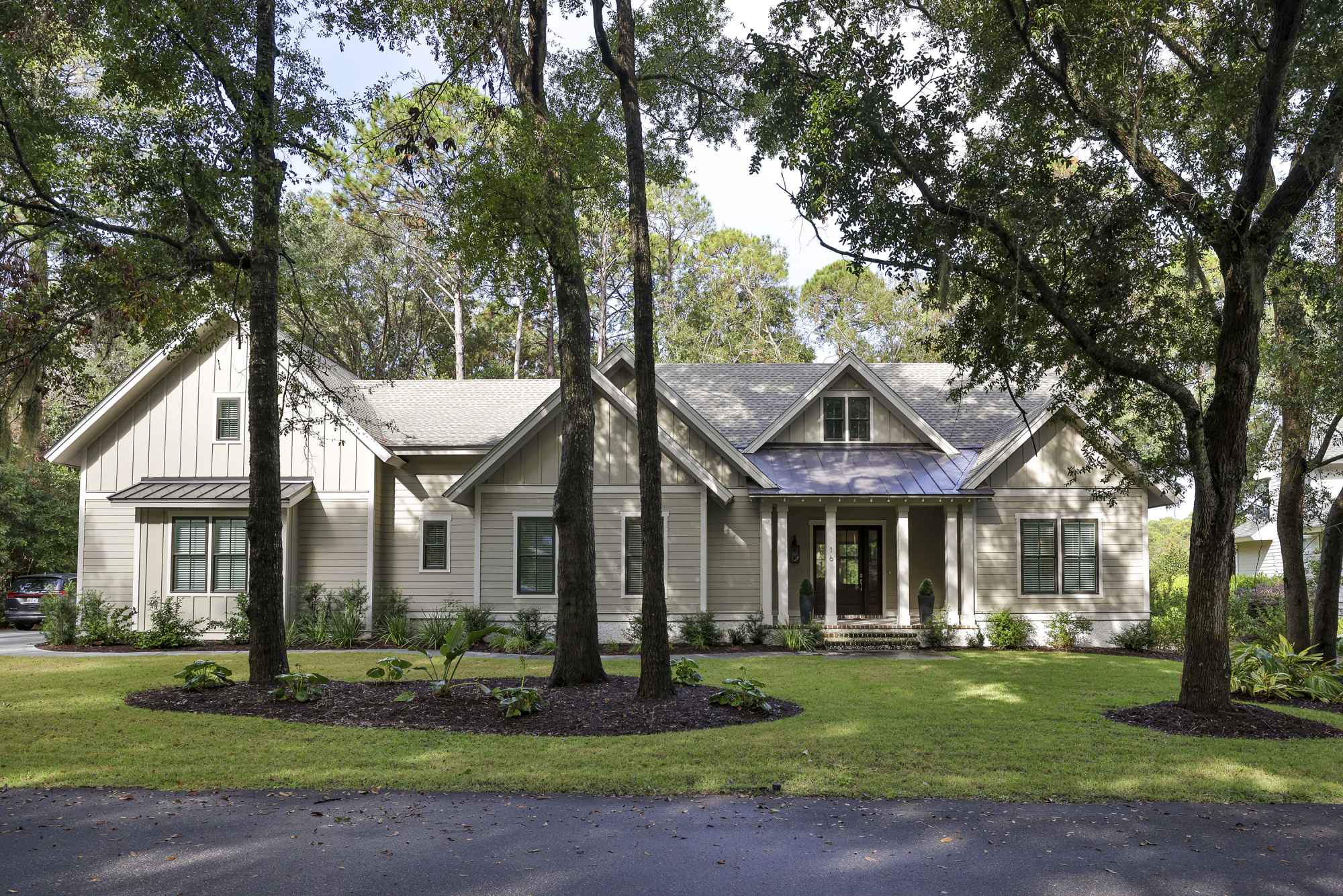 A charming, light gray house with a gabled roof, surrounded by trees and a manicured lawn.
